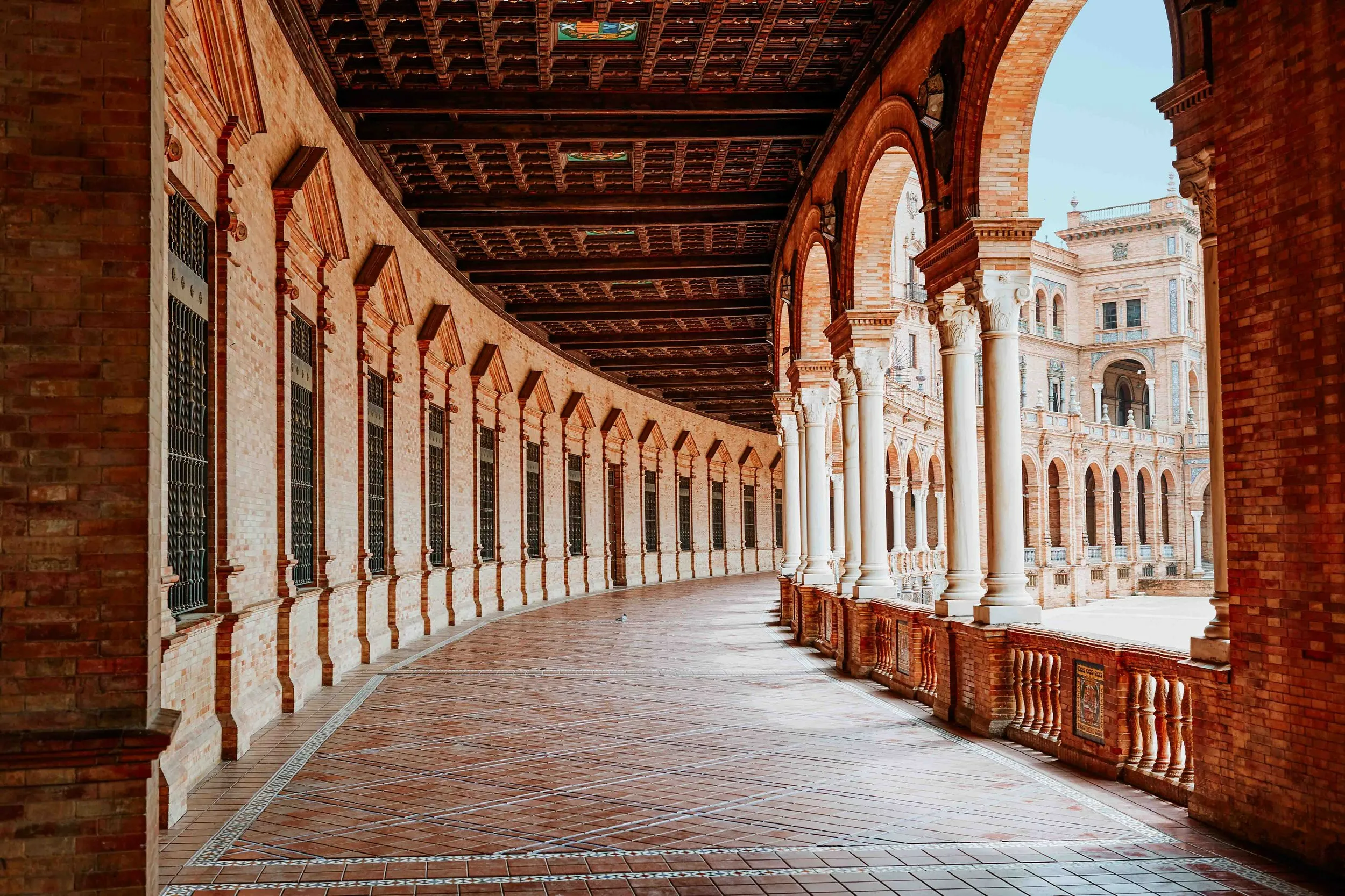 Light filtering through arcades onto patterned tile flooring in palace gallery