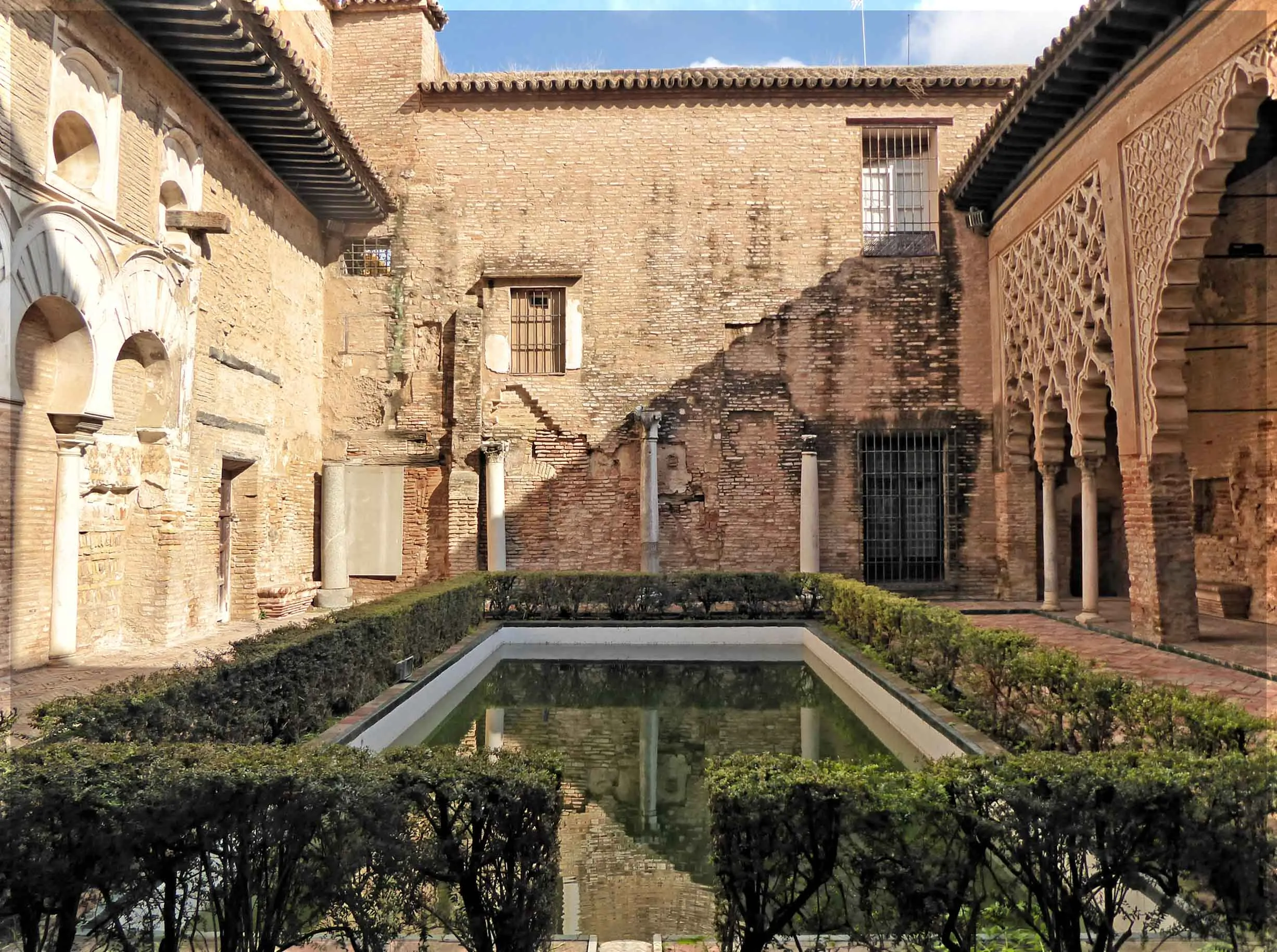 Calm reflective pool capturing arches and lattice patterns inside the Alcázar